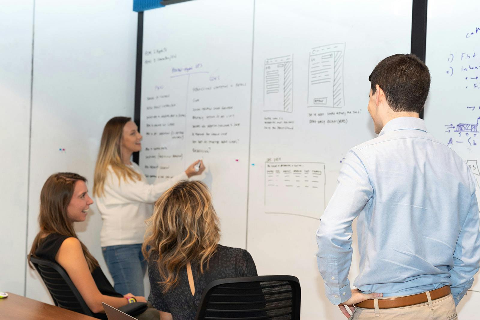 Woman writing on whiteboard with coworkers looking on