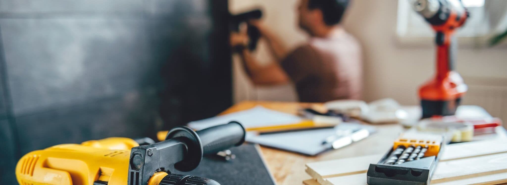 tools in foreground, man nailing wall in background